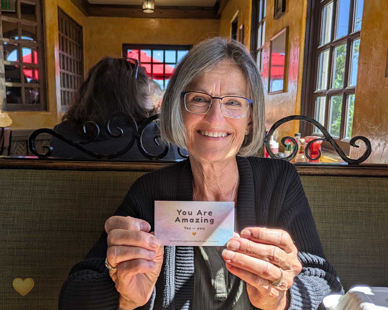 Woman holding a card that says 'You Are Amazing' in a restaurant setting