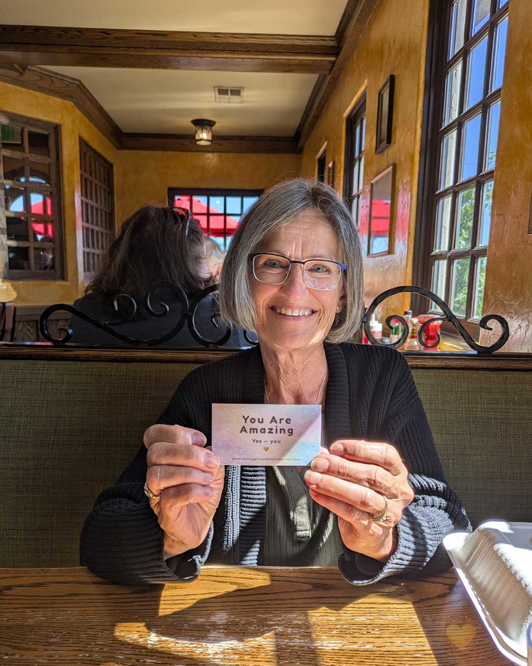 Woman holding a card that says 'You Are Amazing' in a restaurant setting