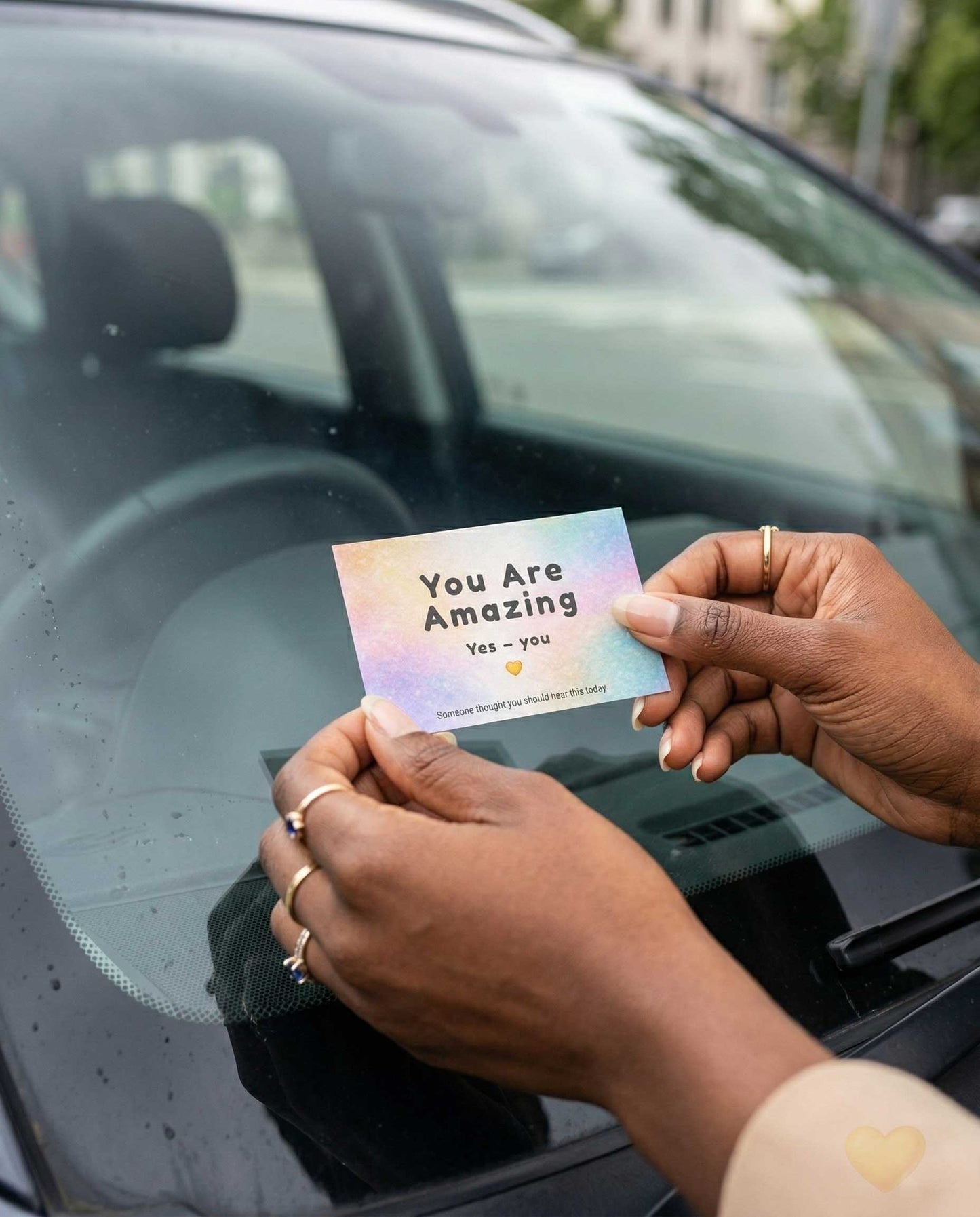 Person holding a card with 'You Are Amazing' message in front of a car window