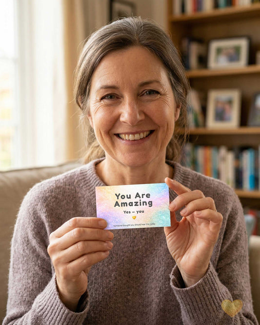 Woman holding a card with 'You Are Amazing' message in a cozy room.